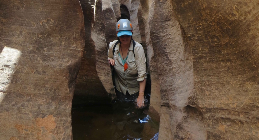 A person makes their way through a narrow canyon in waist-deep water.